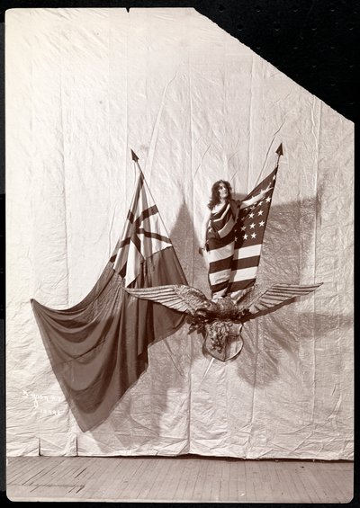 A Living Picture: a model draped in the American Flag standing atop a sculpture of a bald eagle by Byron Company